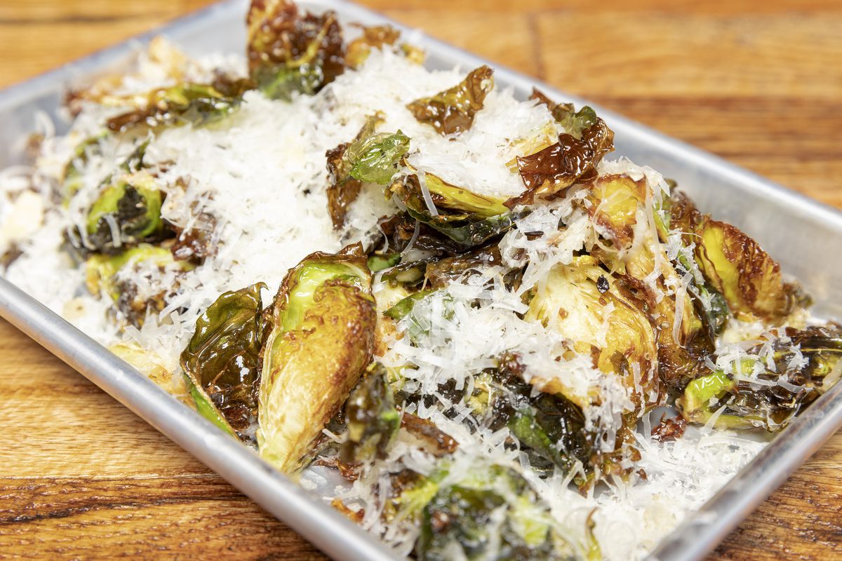 A tray of flash-fried Brussels sprouts covered ina layer of shaved parmesan. 