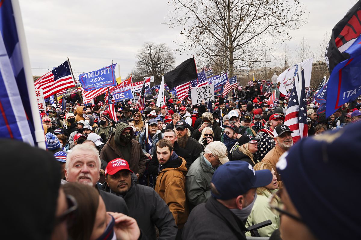 A crowd of people at a pro-Trump rally, waving flags and wearing MAGA hats.