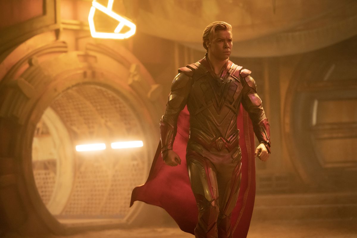 Adam Warlock (played by Will Poulter), a gold-skinned humanoid with gold and red armor and a red cape, strides through a building in Guardians of the Galaxy Vol. 3