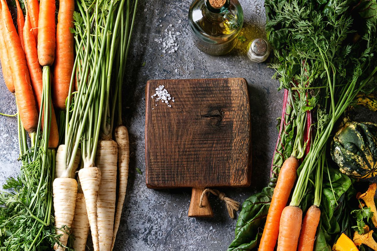 Variety of autumn harvest vegetables carrot, parsnip, chard, paprika, hokkaido pumpkin, mushrooms. Empty wooden chopping board, olive oil, salt over gray texture background. Cooking concept. Top view