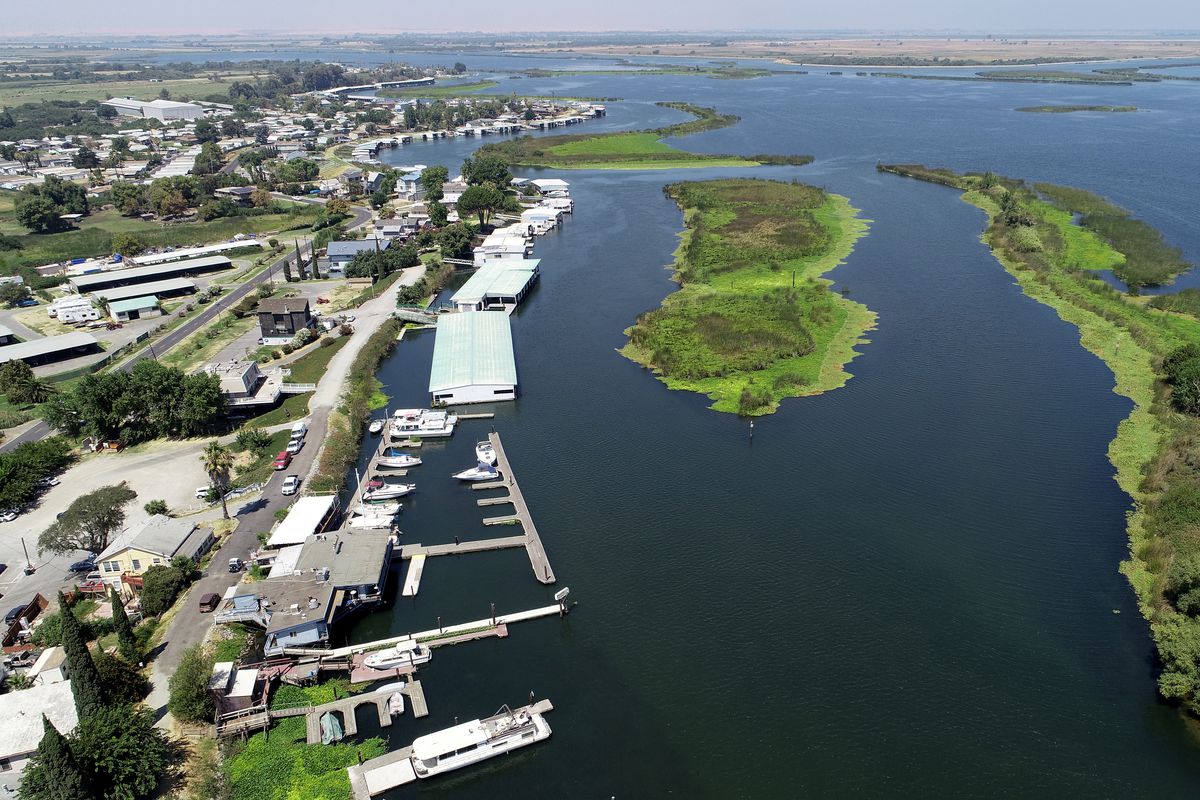 A marina photographed from the air, with white buildings on the left and green, verdant sandbars on the right.