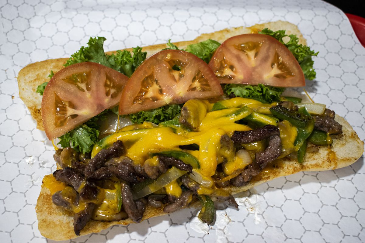 An open cheesesteak with sliced tomatoes, Cheez Whiz, and lettuce.