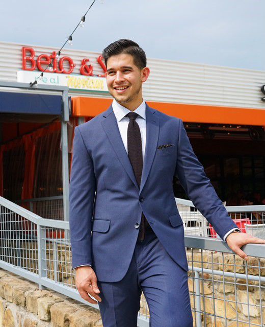 A young Hispanic man in a suit stands outside of a restaurant called Beto &amp; Son.