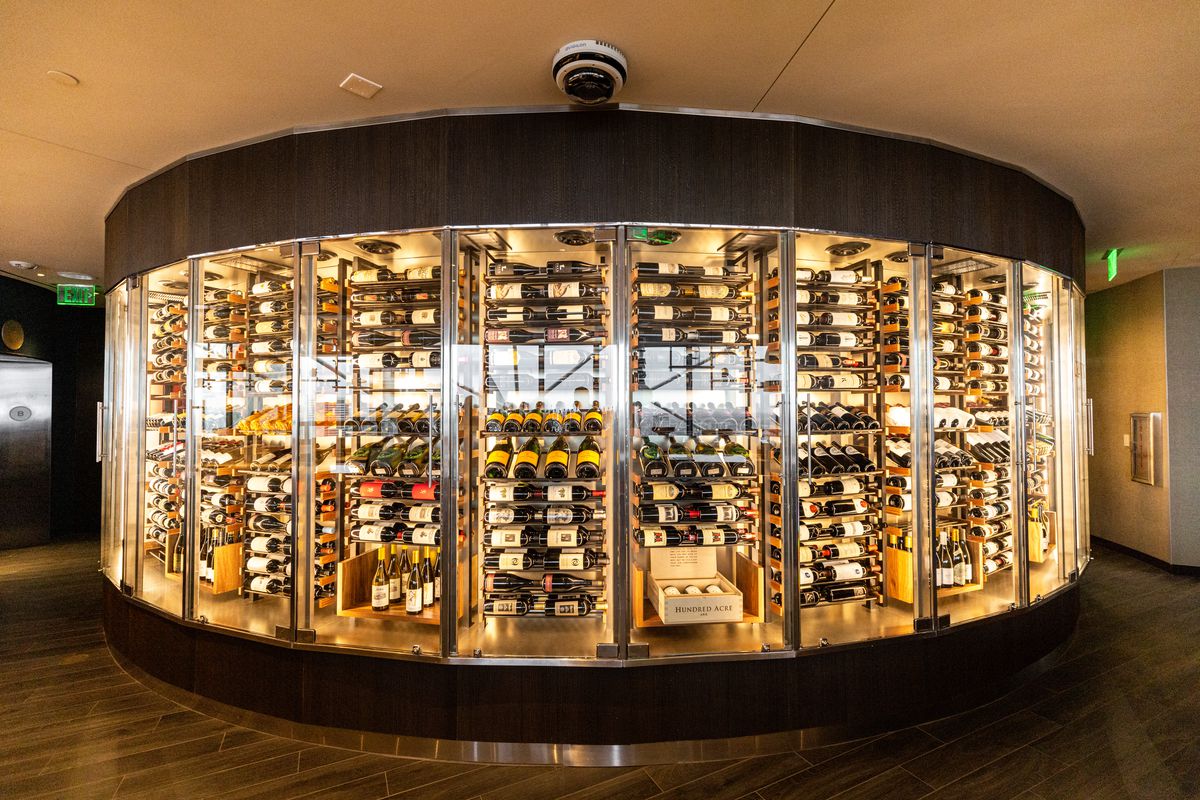A circular, floor to ceiling, glass-door refrigerator holds an uncountable number of bottles of wine.