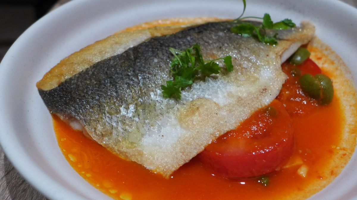 A crisp fish filet in a sauce with sliced tomatoes.