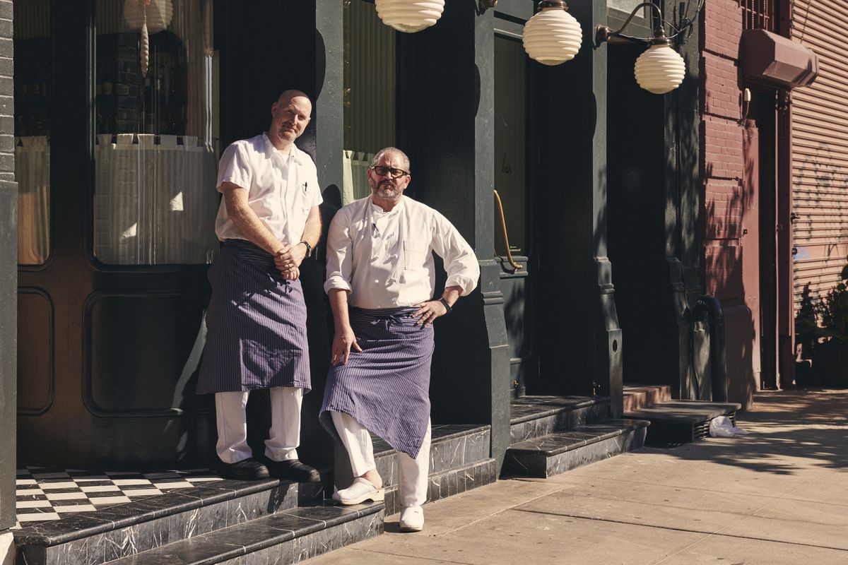 Chefs Lee Hanson and Riad Nasr stand in front of Frenchette, a restaurant that has a black painted front