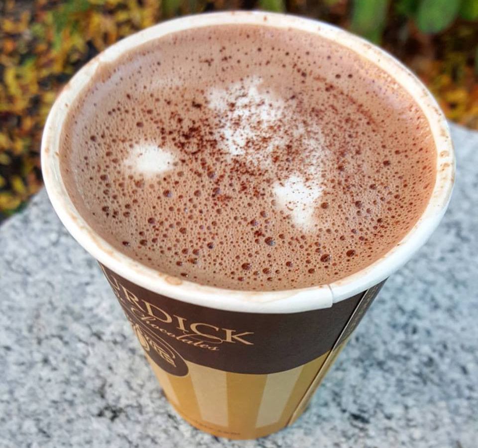A frothy hot chocolate in a to-go cup sits on a stone surface