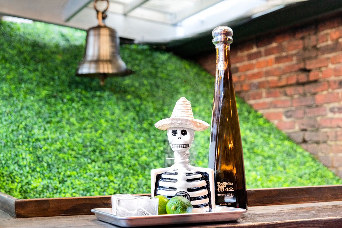 A bottle of Don Julio 1942 next to a skeleton figurine and frozen shot glasses with a bell and greenery in the background