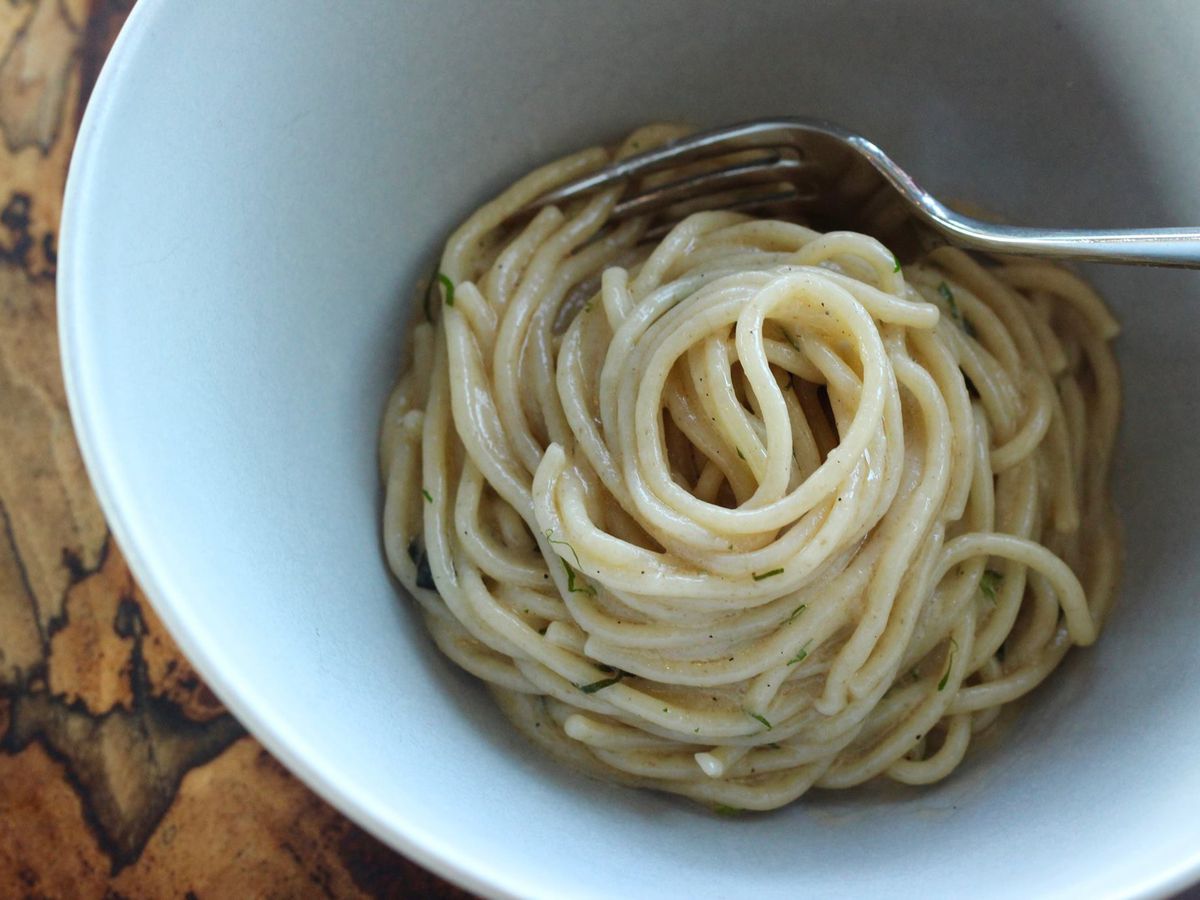 A bowl of pale yellow spaghetti pasta with a fork in it.