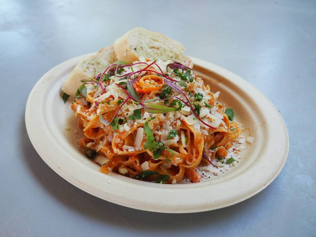 A dish of red pasta topped with shaved white cheese and green garnishes, served with slices of garlic bread.