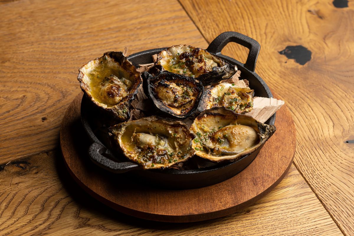 A dark bowl of charred oysters over wood.