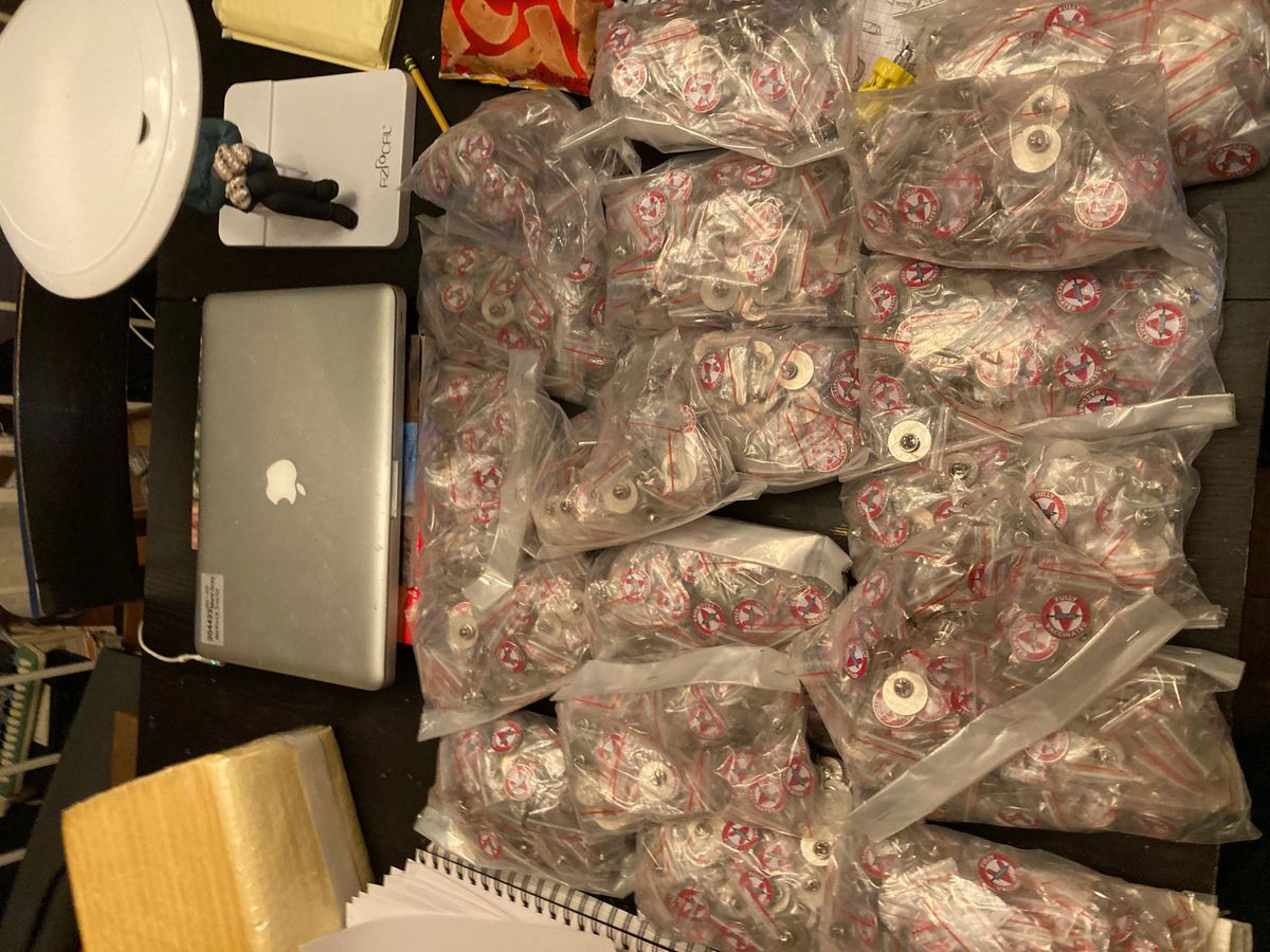 Plastic bags full of identical vaccine pins, on a desk with a laptop computer.