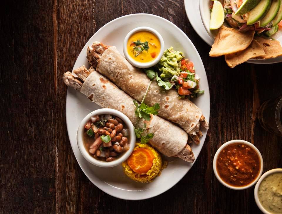 A plate of soft, rolled tacos with beans, guacamole, and salsas.