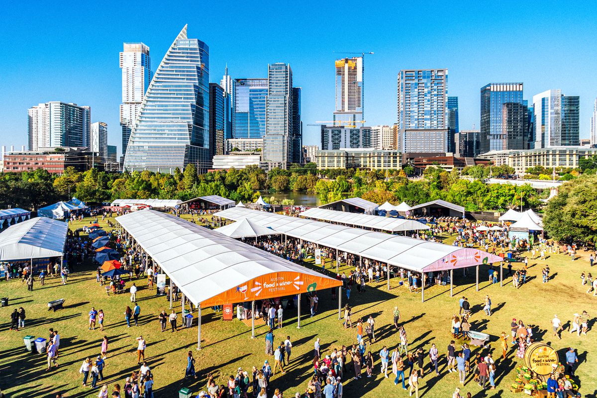 An aerial shot of a food festival in front of a city skyline with tents and people.