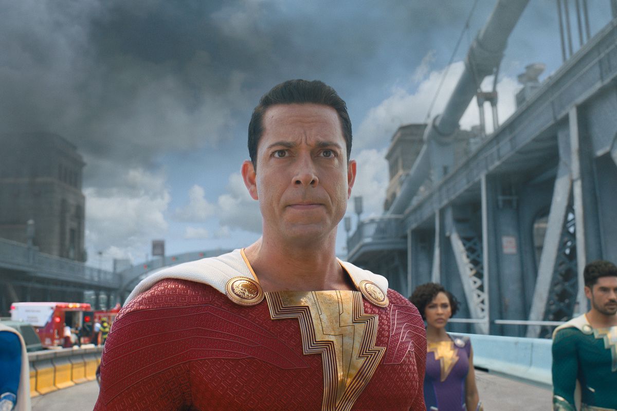Shazam and his superhero family stand on a burning bridge looking at a threat offscreen in Fury of the Gods
