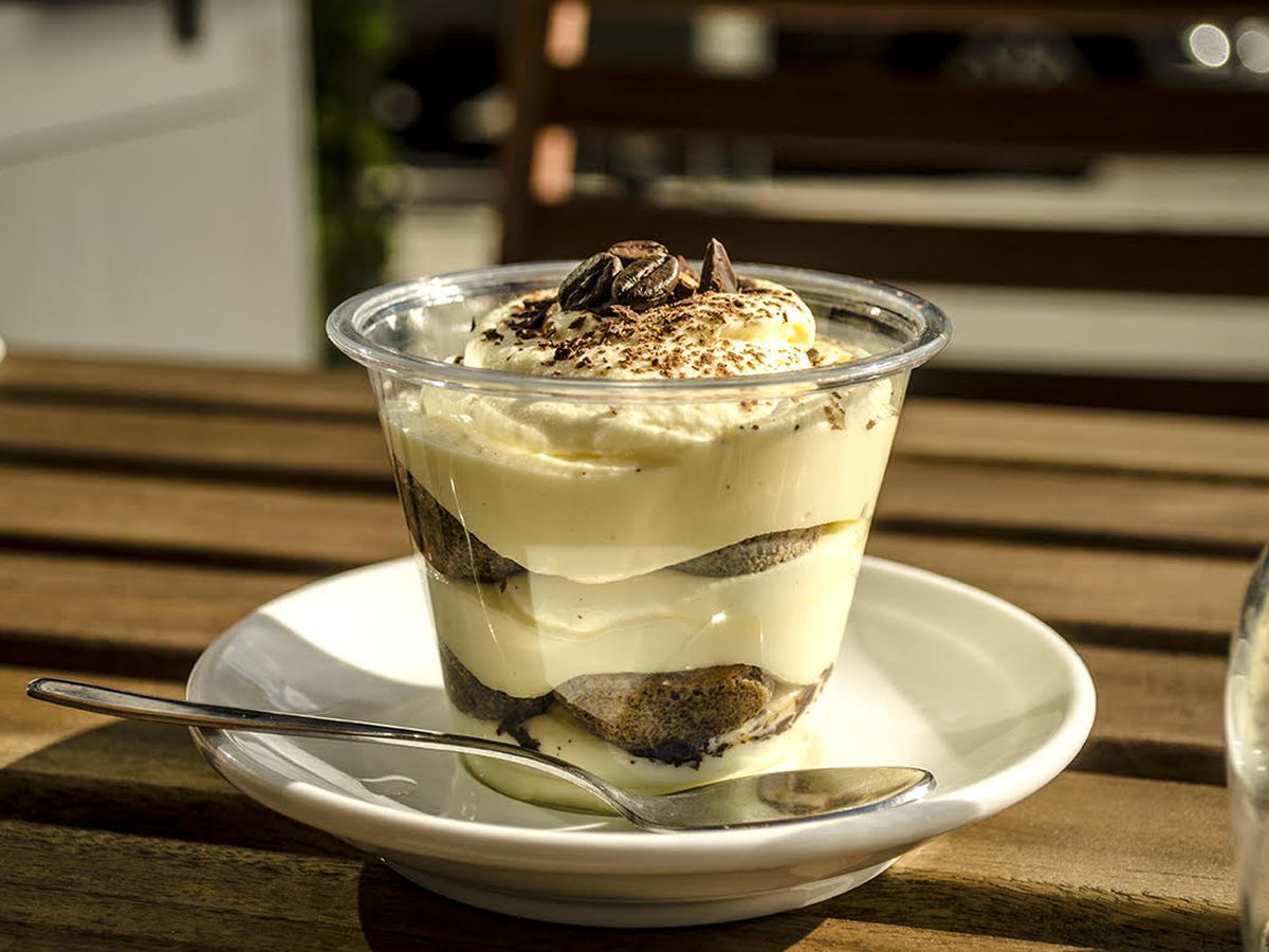 A cup of tiramisu sitting on a small white saucer placed on a wooden table.