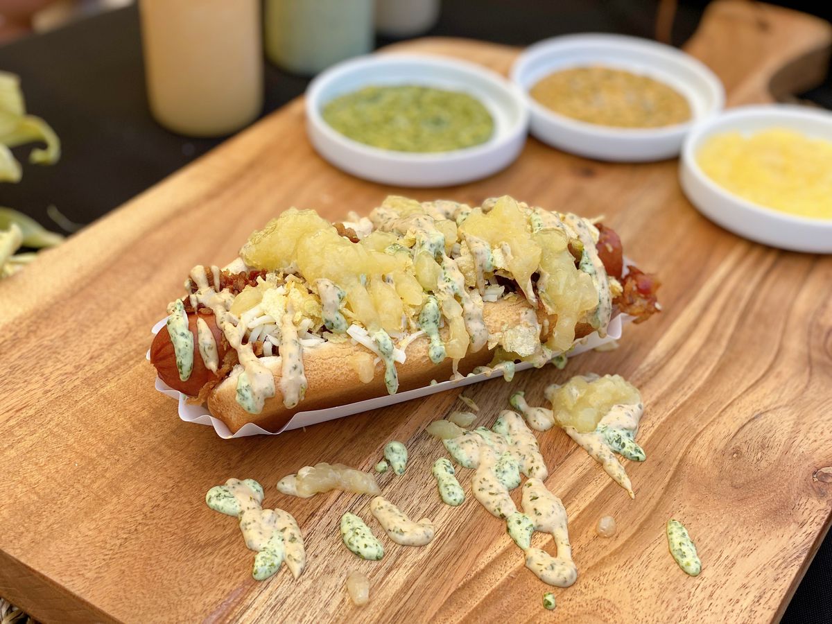 Colombian-style hot dog from WezzArepas sauced up on a wooden board.