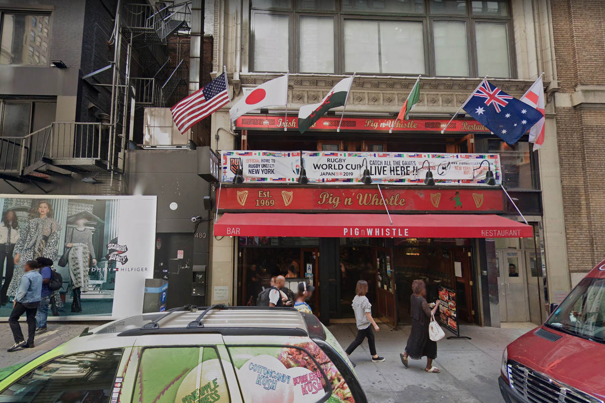The front of a building with an Irish pub decked out with country flags and a red awning located at the ground floor