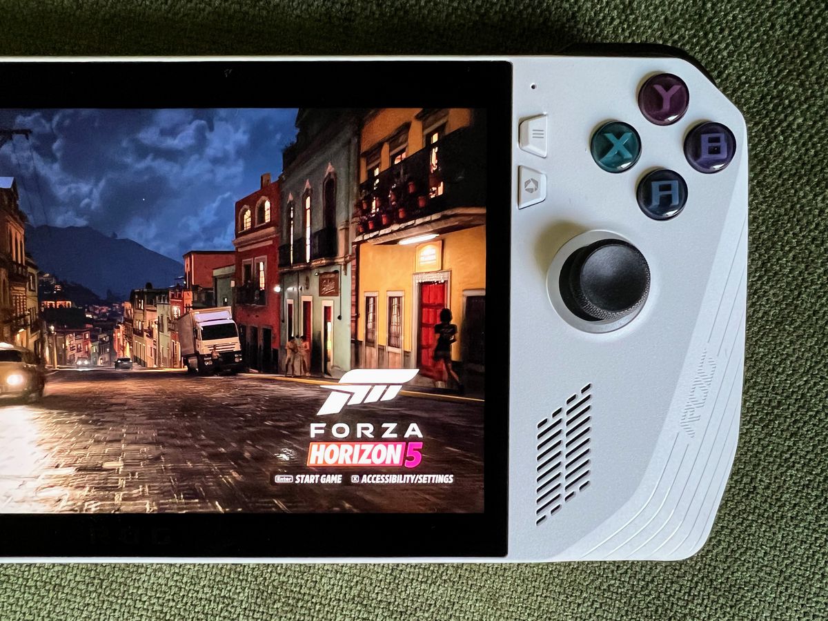 a rainy street scene in Forza Horizon 5 running on an Asus ROG Ally gaming handheld, lying on olive green fabric, in a close-up overhead photo of the right side of the device
