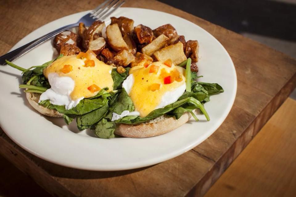 A sunny plate of poached eggs, Hollandaise sauce, and arugula on a white plate and wooden table at Overland Cafe.