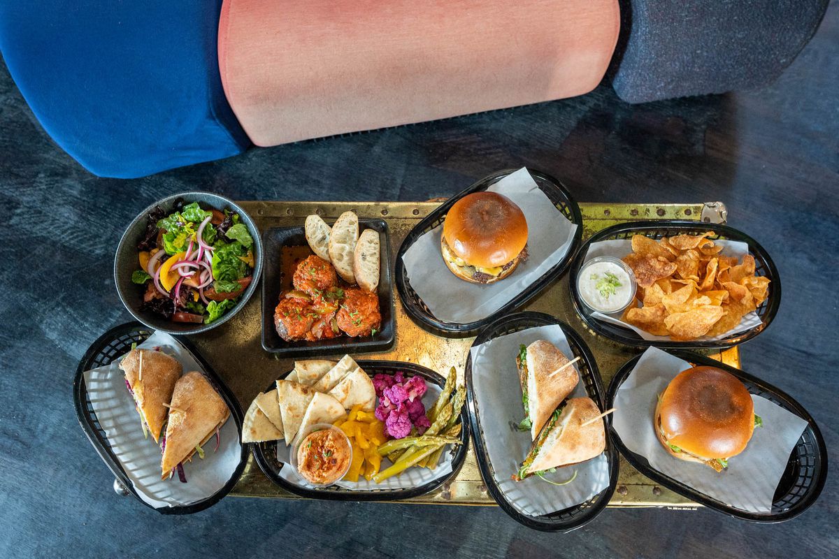 A couple of burgers, sandwiches, meatballs, and some fried items laid out on a table.