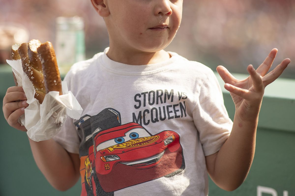 A young fan in the bleachers holds a soft pretzel and reacts during a game between the Kansas City Royals and the Boston Red Sox on September 18, 2022 at Fenway Park in Boston, Massachusetts.