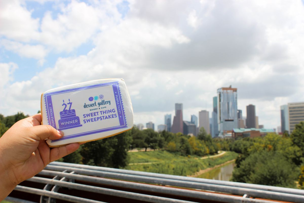 A person holds up purple and white cookie ticket in front of views of Houston’s Downtown skyline.