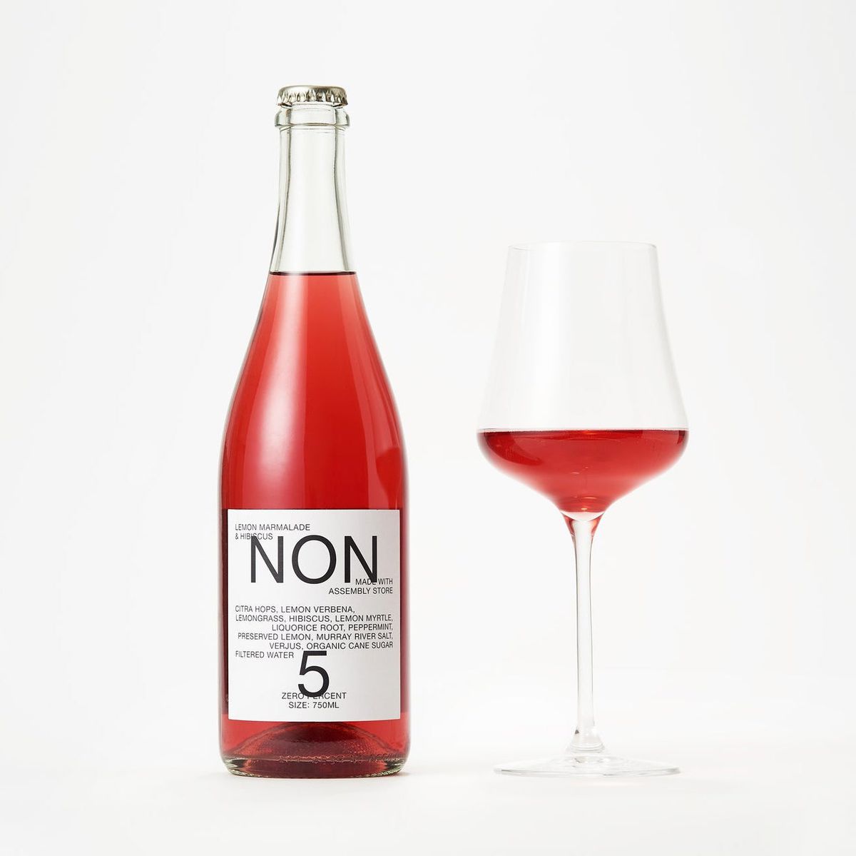 A bottle of red beverage with a white label that reads “NON 5” next to a glass filled with the same beverage.