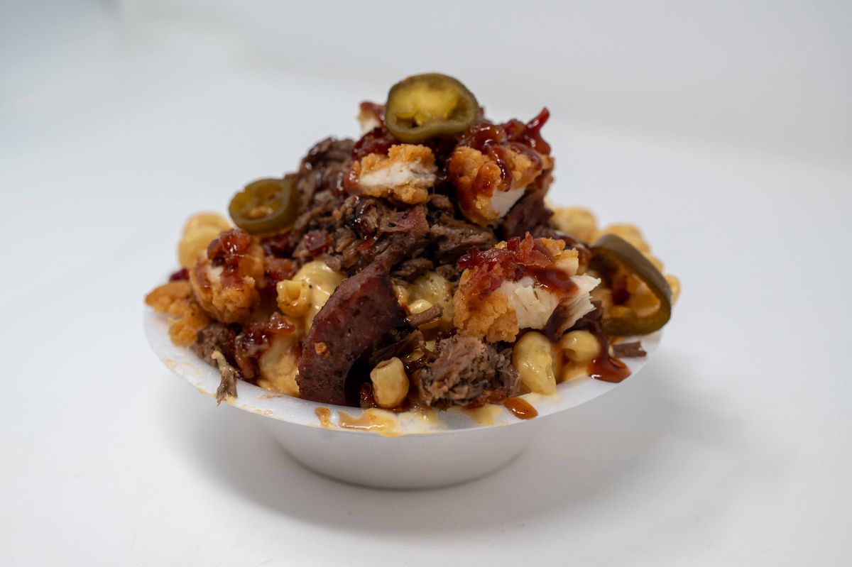 A bowl holds mac and cheese, fried chicken, brisket, sausage, and candied bacon.