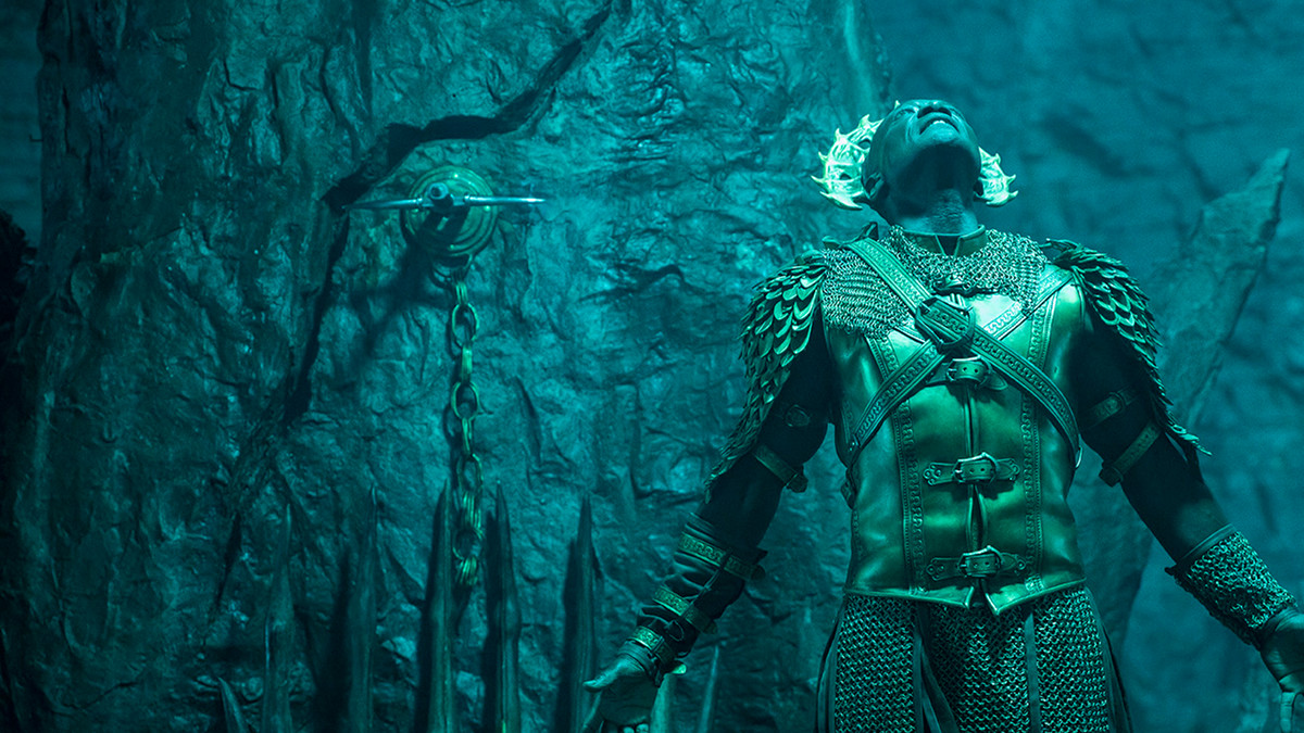 Peter Mensah as the Archangel Michael, staring up at unknown light source with a stone wall in the background in The Devil Conspiracy.