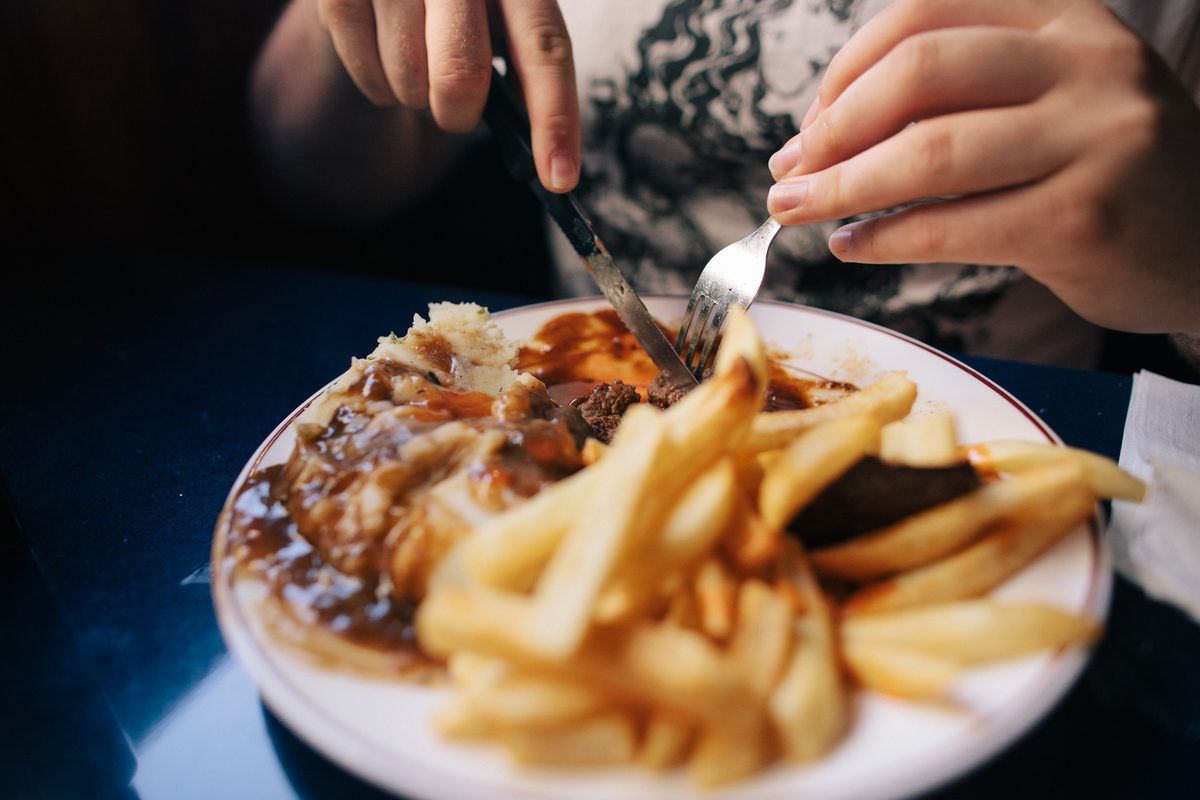 A patron at South Street Diner cuts into food on a plate, with a pile of fries in the foreground