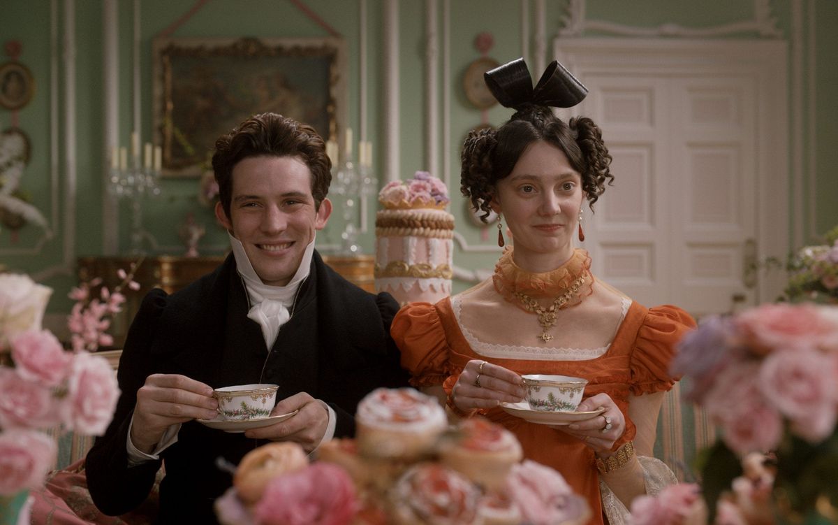 Mr. Elton (Josh O’Connor) and Mrs. Elton (Tanya Reynolds) sit for tea amidst a bunch of flowers.