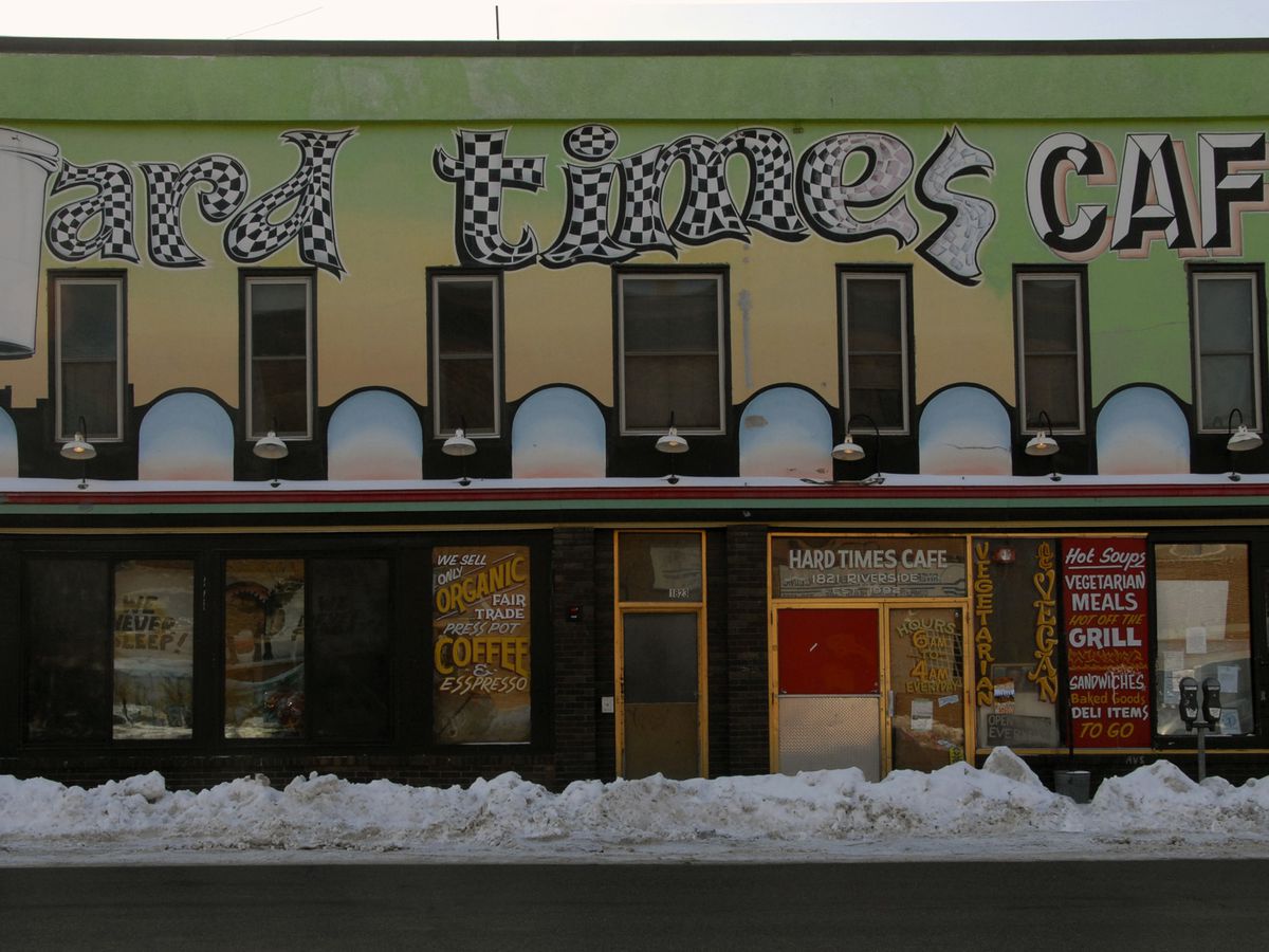 The exterior of the Hard Times Cafe, which is painted green and yellow with white a black block lettering. There is a snowbank in front of it. 
