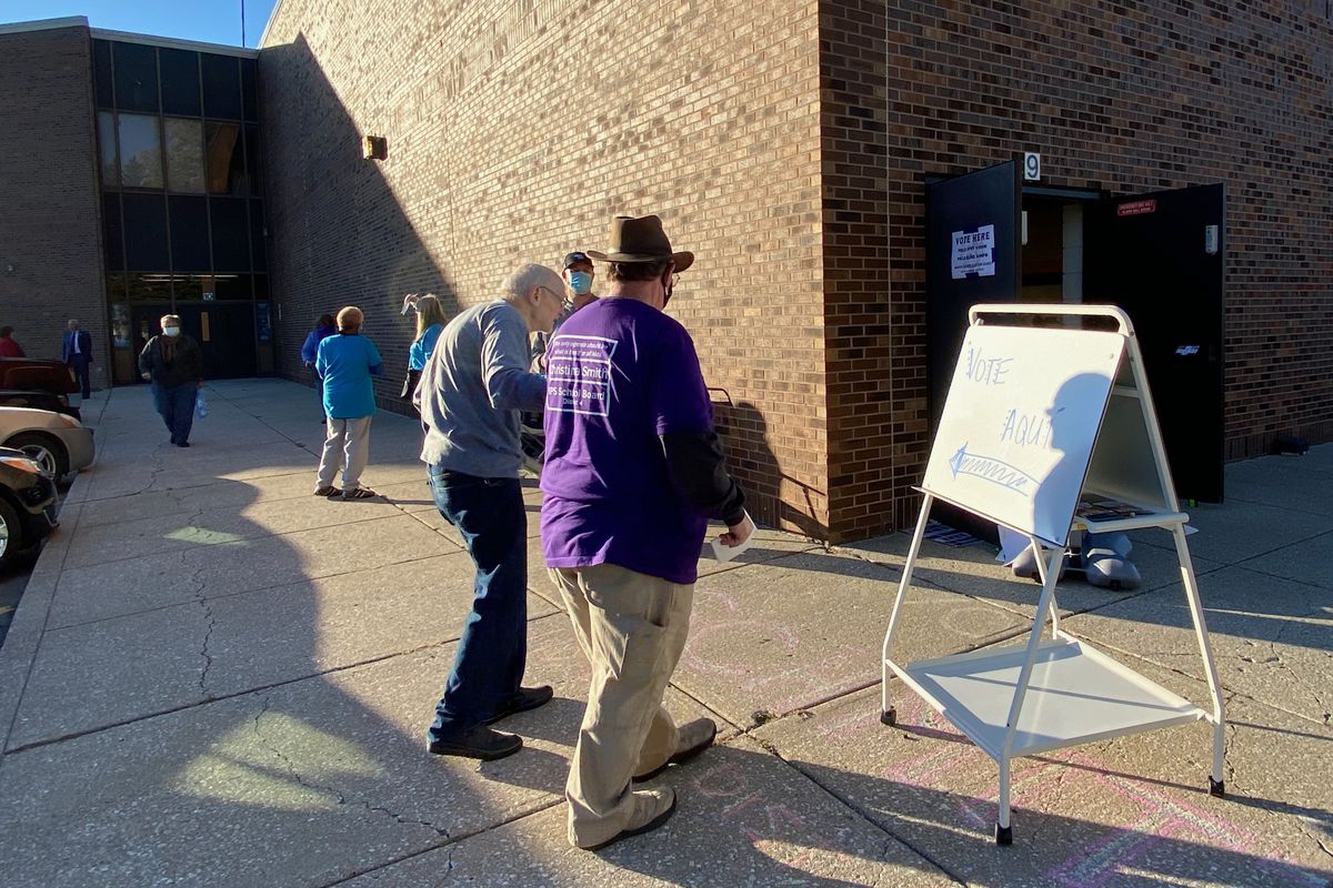A campaign worker helps walk a man past a sign on an easel on a patio outside a polling station.