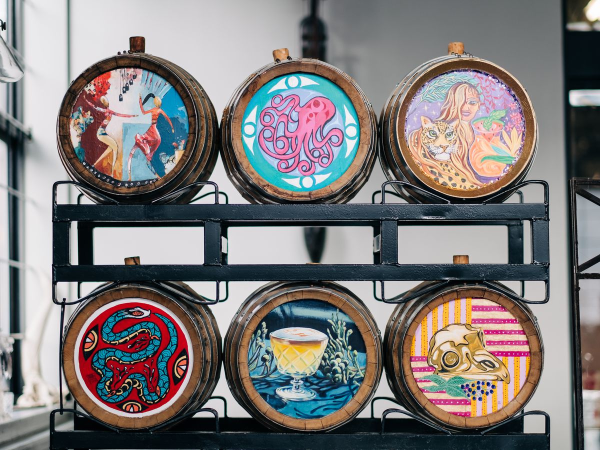 Barrels for aging spirits decorated with various illustrations on a rack in an industrial space