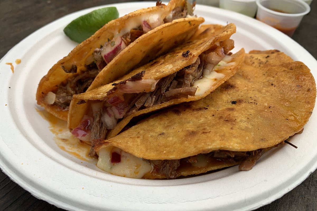 Three birria tacos on a paper plate, with a wedge of lime