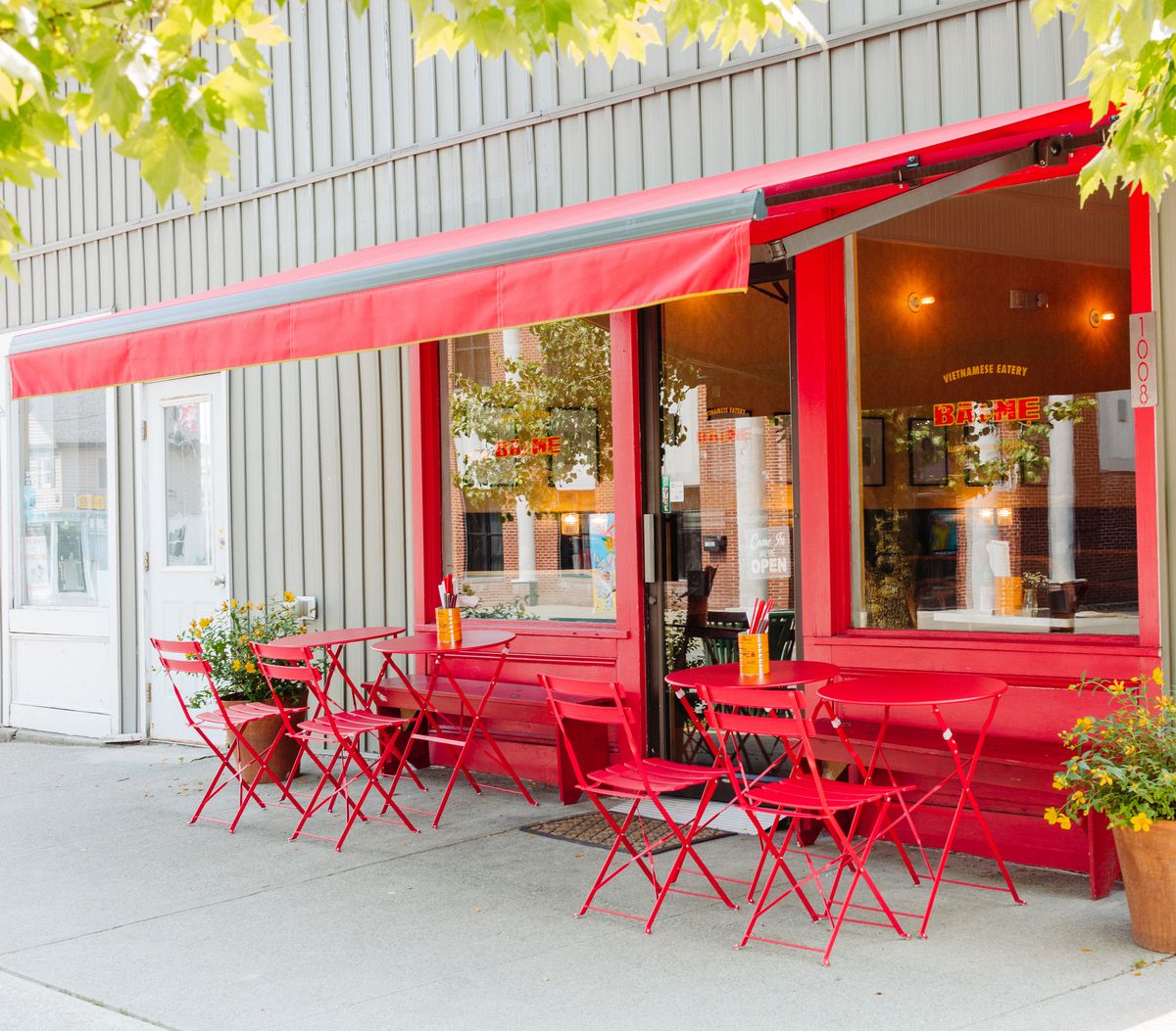 A bright red restaurant exterior, with red awning and red metal tables and chairs. 