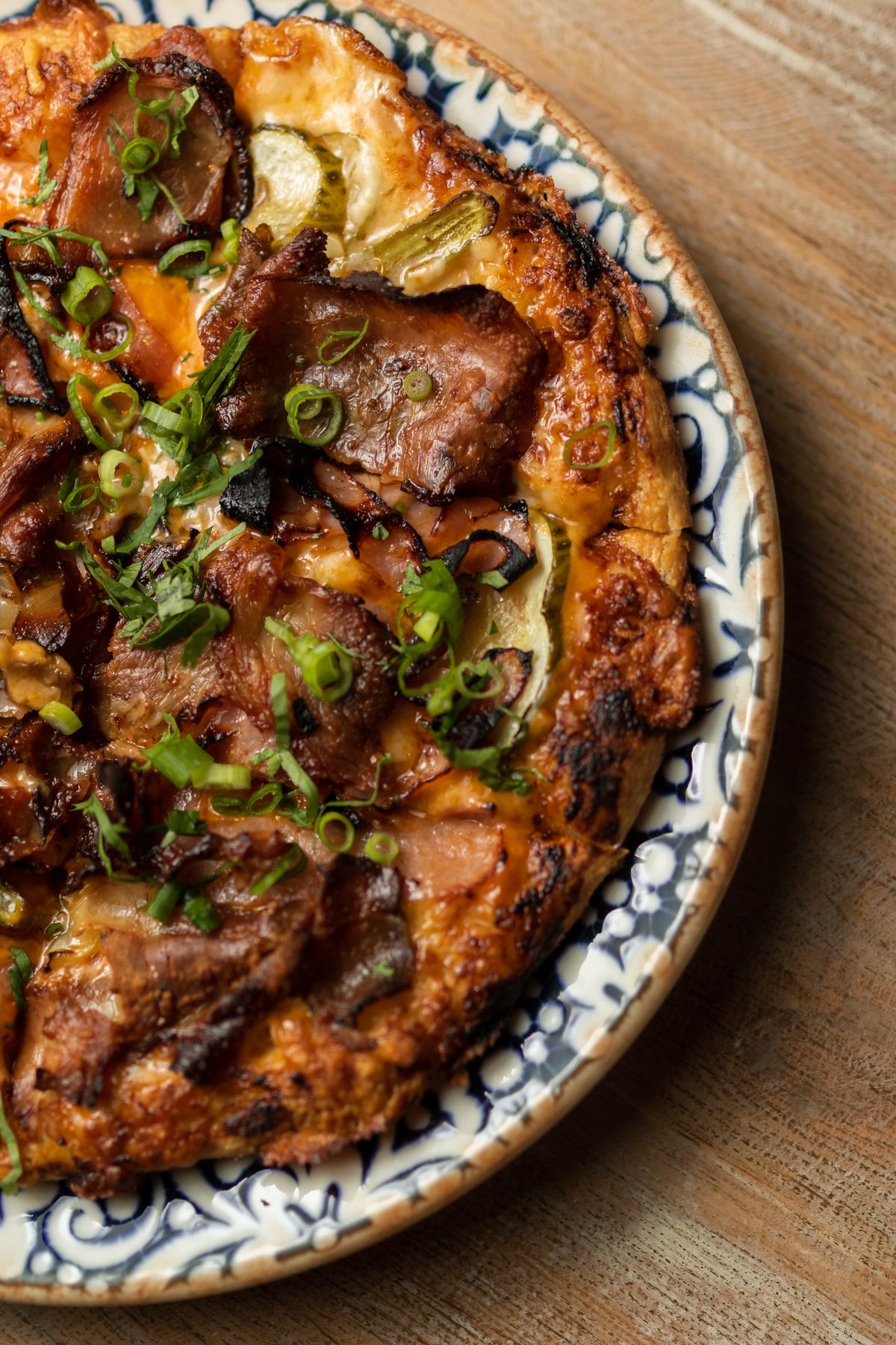 A crispy Cuban street pizza topped with lechon sits on a plate with a blue and white pattern
