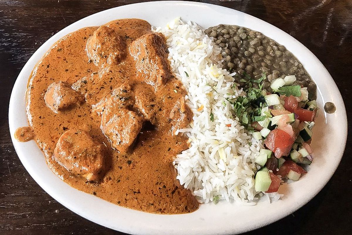 An overhead shot of butter chicken and rice shown on a heavy white plate.