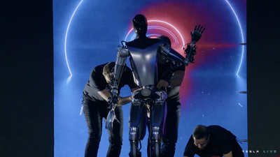 A picture of a Tesla robot being supported on stage by three engineers.