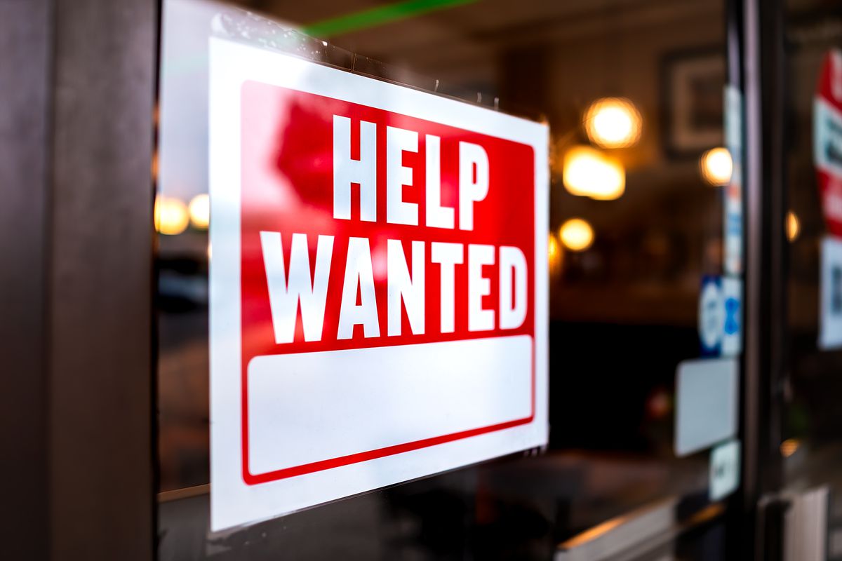 A red and white help wanted sign hangs in the window