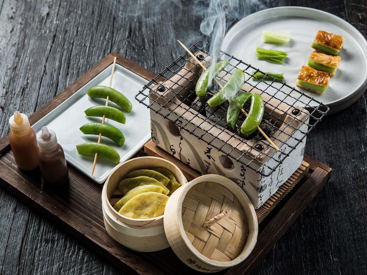 A grill with skewers of green vegetables are displayed along a steamed basket.