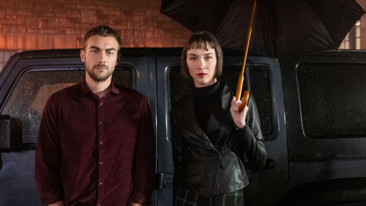 Tom Austen and Sydney Lemmon stand in front of a black van and glower as Daimon and Ana Helstrom in Helstrom