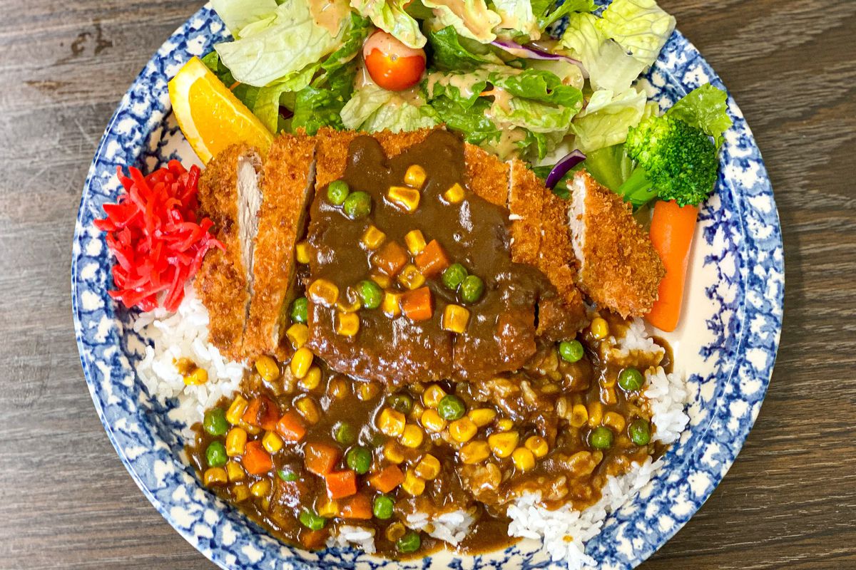Japanese curry with pork over rice with vegetables on a traditional blue plate.