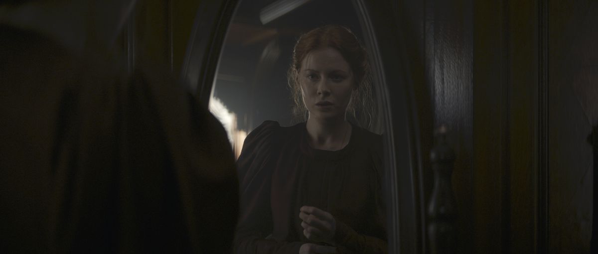 A distressed Maura (Emily Beecham) looks at her reflection in a mirror in 1899.