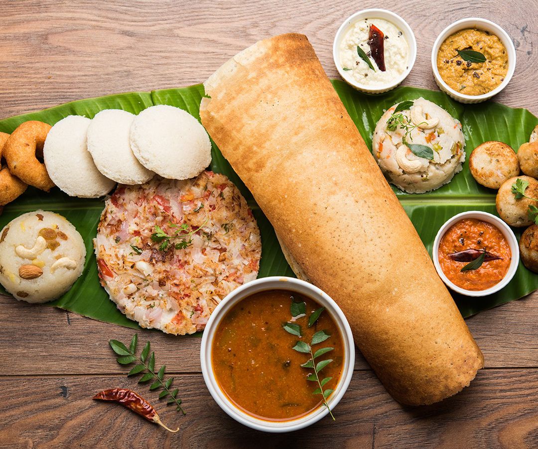 From above, a variety of dishes centered around a large dosa, set on a large leaf on a wood table
