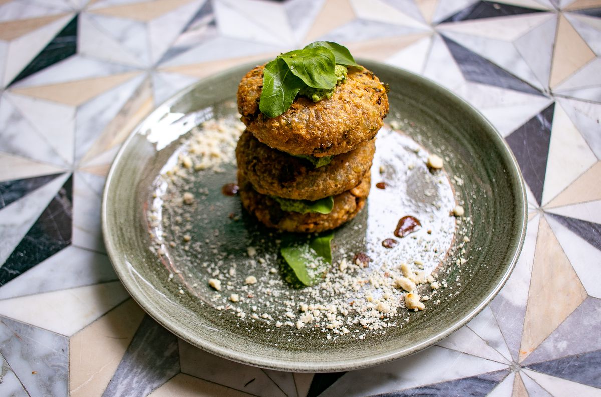 A light green round plate with three brown fritters stacked on top of each other with a spoonful of green chutney placed between each fritter.