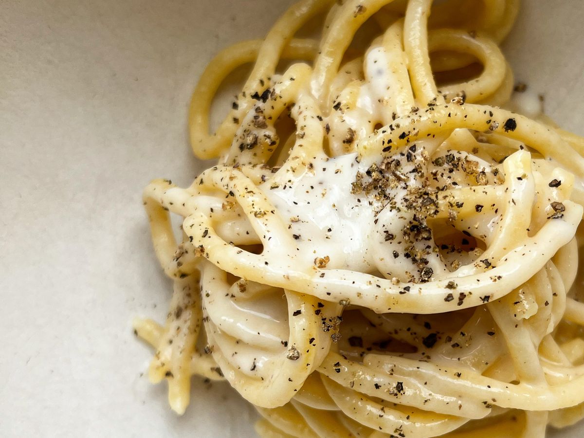 A closeup on a bowl of pasta topped with visible grains of pepper and cheese.