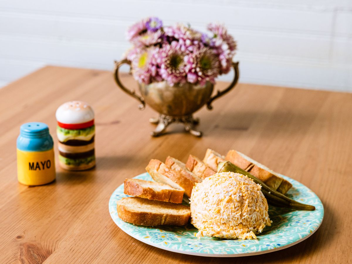 A scoop of pimento cheese on a blue plate, surrounded by bread. 