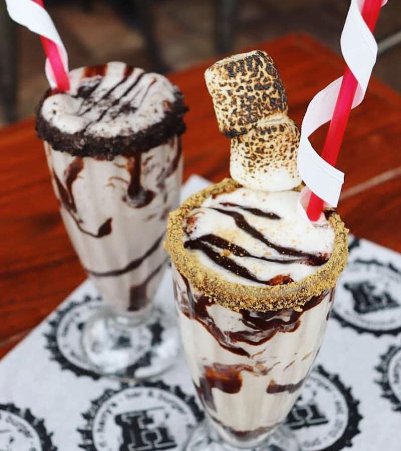 Two milkshakes topped with chocolate sauce, toasted marshmallows, and crumbled graham cracker rims